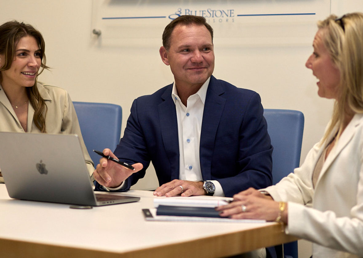 Three business professionals having a discussion around a table with a laptop and documents.
