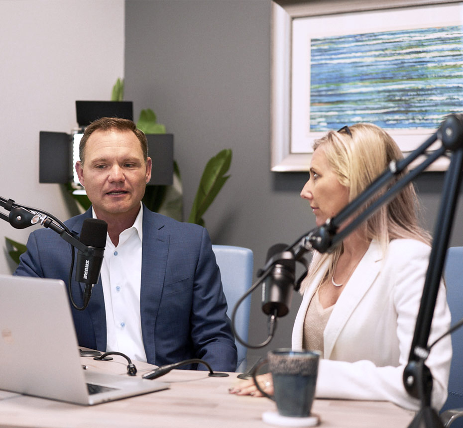 Two professionals recording a podcast or discussion with microphones and a laptop.