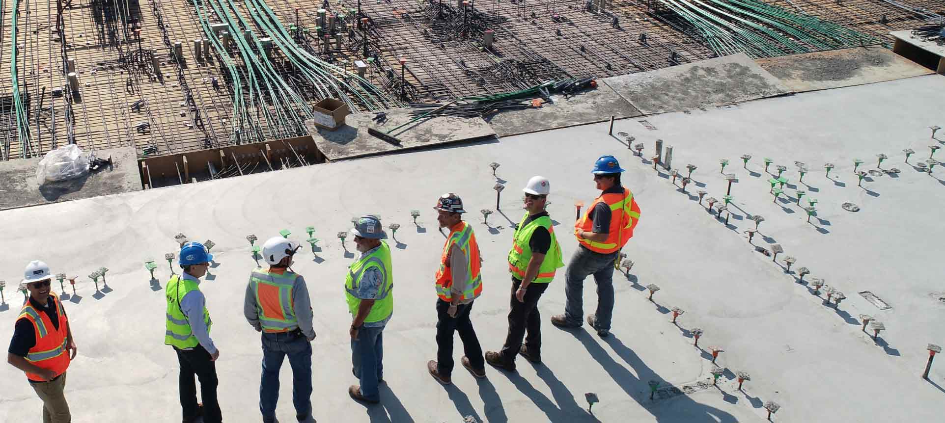 Construction workers standing on a building site, inspecting concrete and rebar installation.