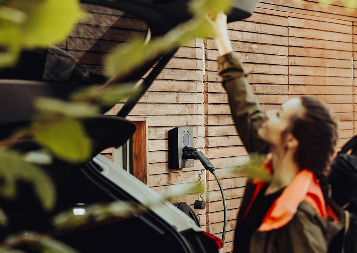 Person charging an electric vehicle at a residential home, representing modern insurance considerations and smart technology adoption.